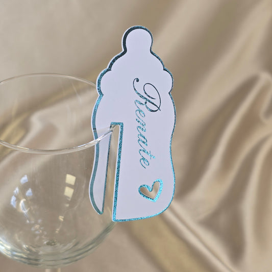 Hvitt bordkort med gjestens navn i folie for dåp, navnefest eller babyshower, formet som en tåteflaske.
